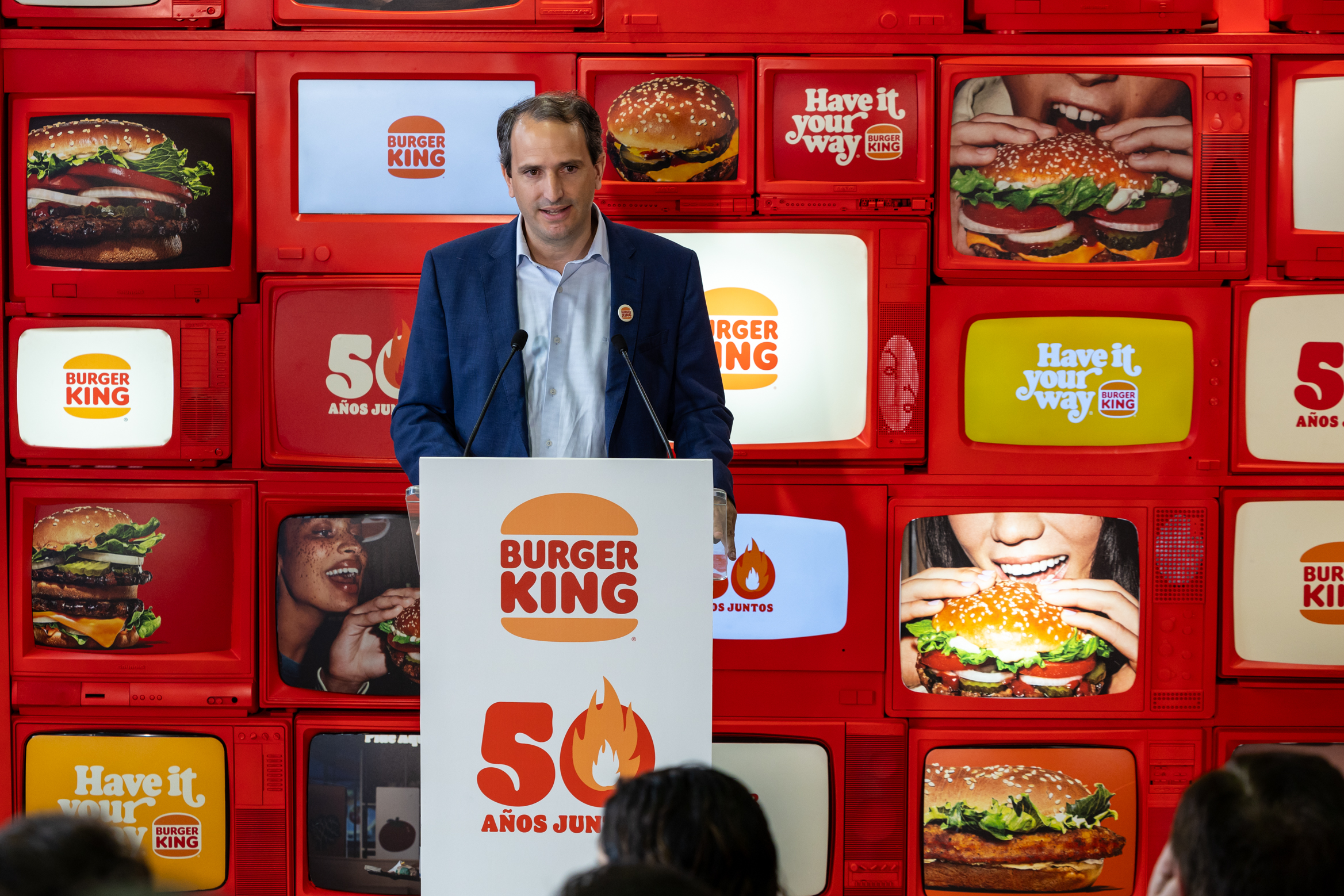 una imágen de Borja Hernández de Alba, CEO de RBE en un atril dando una rueda de prensa por los 50 años de Burger King